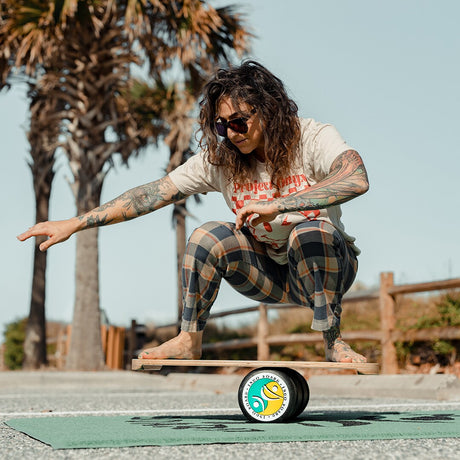 Person balanserar i en låg squat på en Indoboard Ying Yang med roller på en matta utomhus