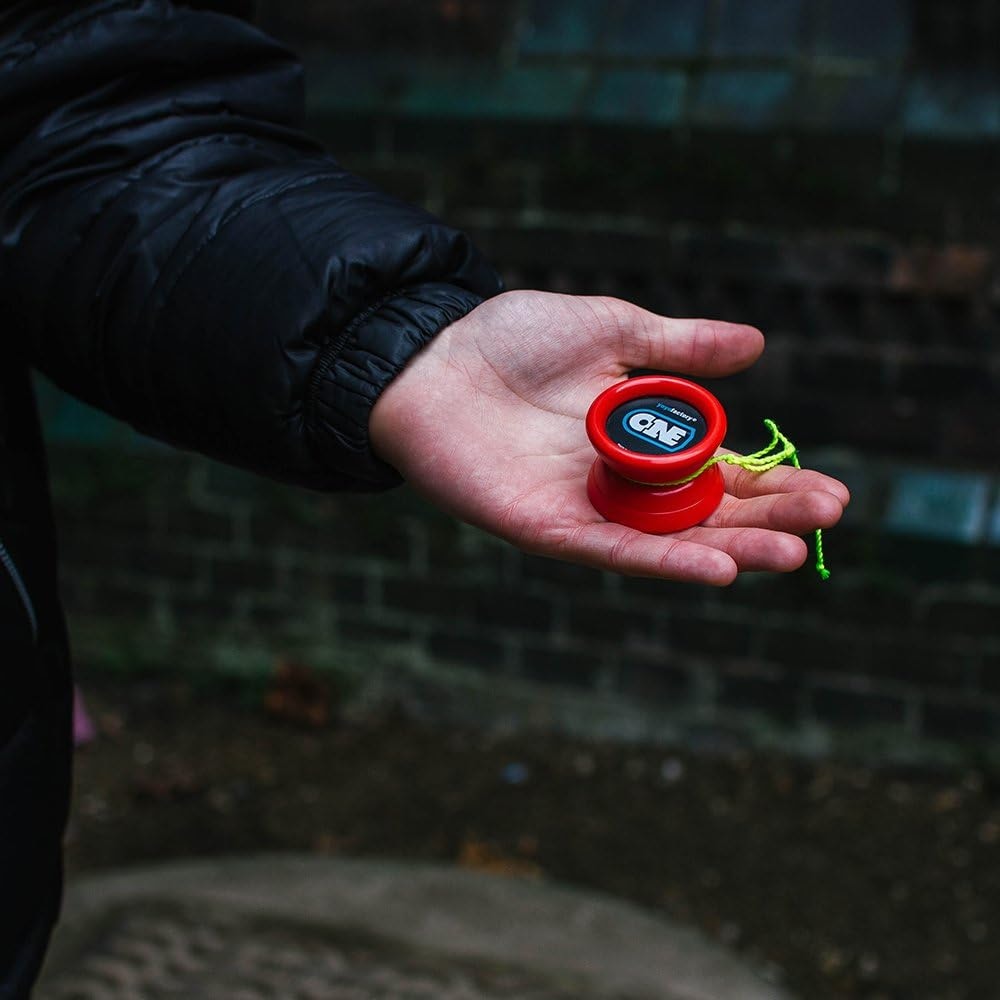 Närbild på en röd YoYoFactory One som ligger i en handflata utomhus. Jojon har en svart och blå logotyp med texten "ONE" och ett neongrönt snöre är lindat runt den.