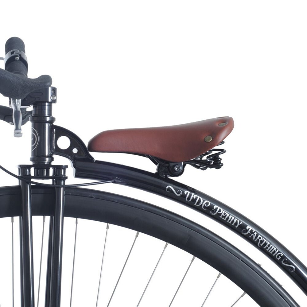 Närbild på den svarta ramen av UDC Penny Farthing, visar den bruna lädersadeln med fjädrar och styrets placering ovanför det stora framhjulet